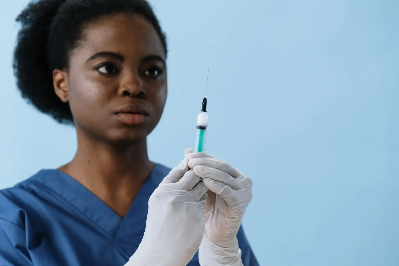 Nurse in scrubs and gloves preparing a vaccine syringe